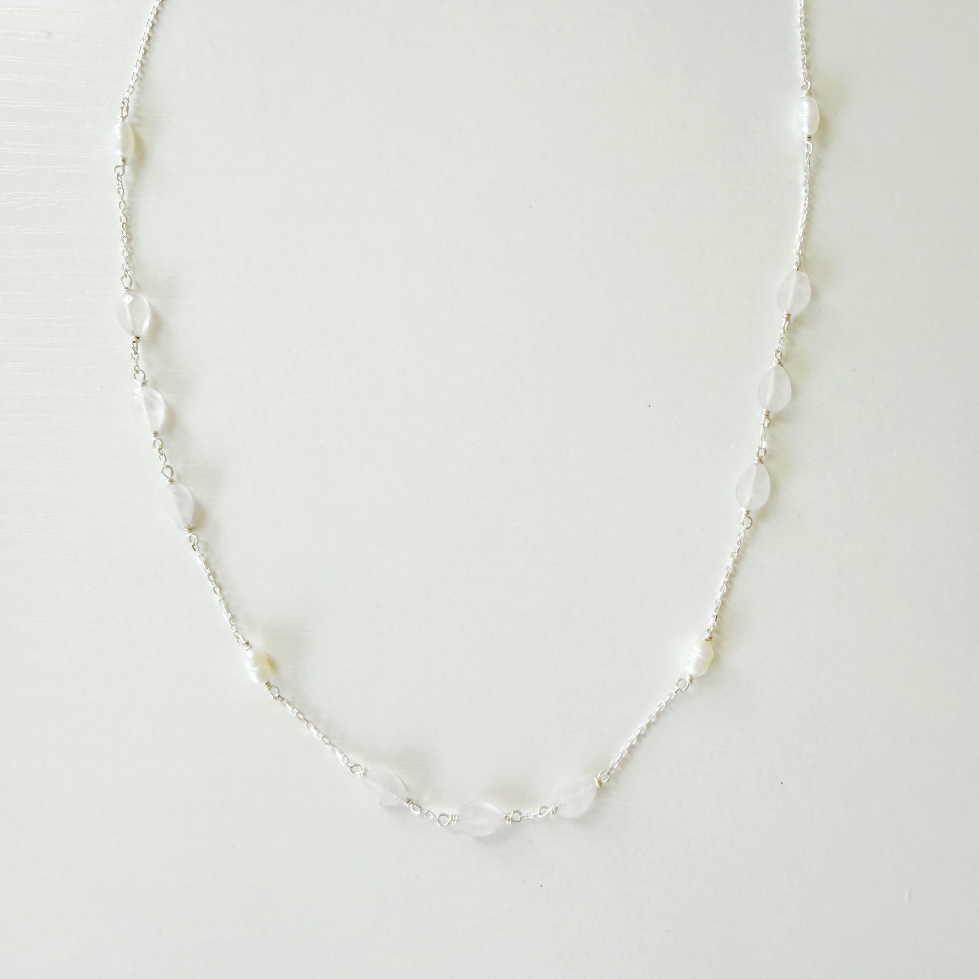 A delicate silver-toned chain necklace featuring small, irregular white pears and light pink kunzite beads spaced along the chain, displayed against a plain white background.
