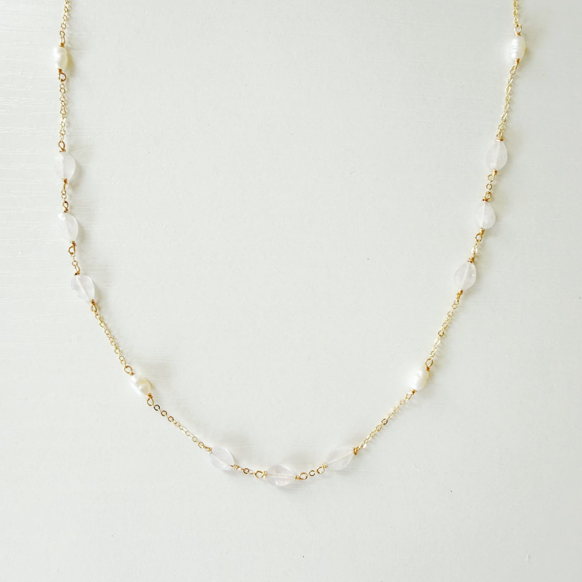dainty 14k gold filled chain necklace with white irregular pearls and light pink kunzite beads spaced out on the necklace. necklace is photographed on a white surface