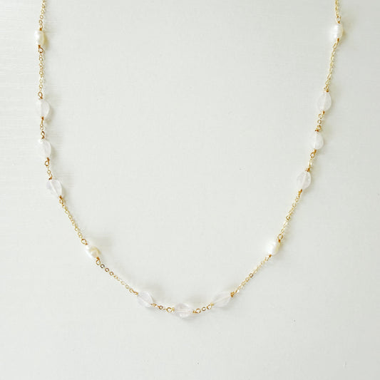 dainty 14k gold filled chain necklace with white irregular pearls and light pink kunzite beads spaced out on the necklace. necklace is photographed on a white surface