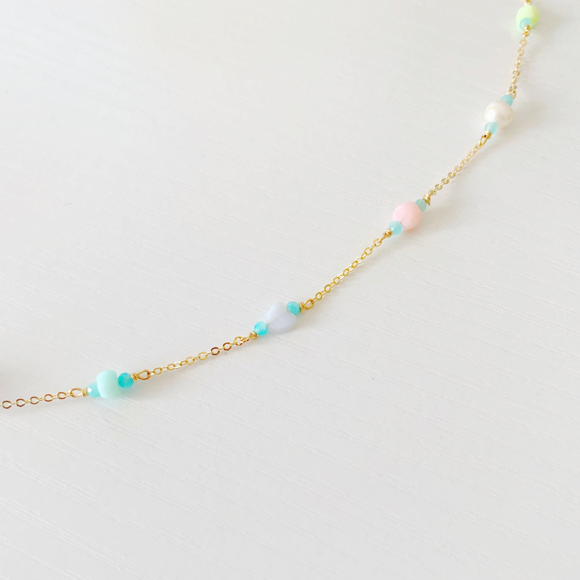 the island hopper necklace by mermaids and madeleines is a station style necklace with a shell at the center and semiprecious beads going up the 14k gold filled chain. this is a detail shot of the necklace that shows one side of the semiprecious beads on a white surface