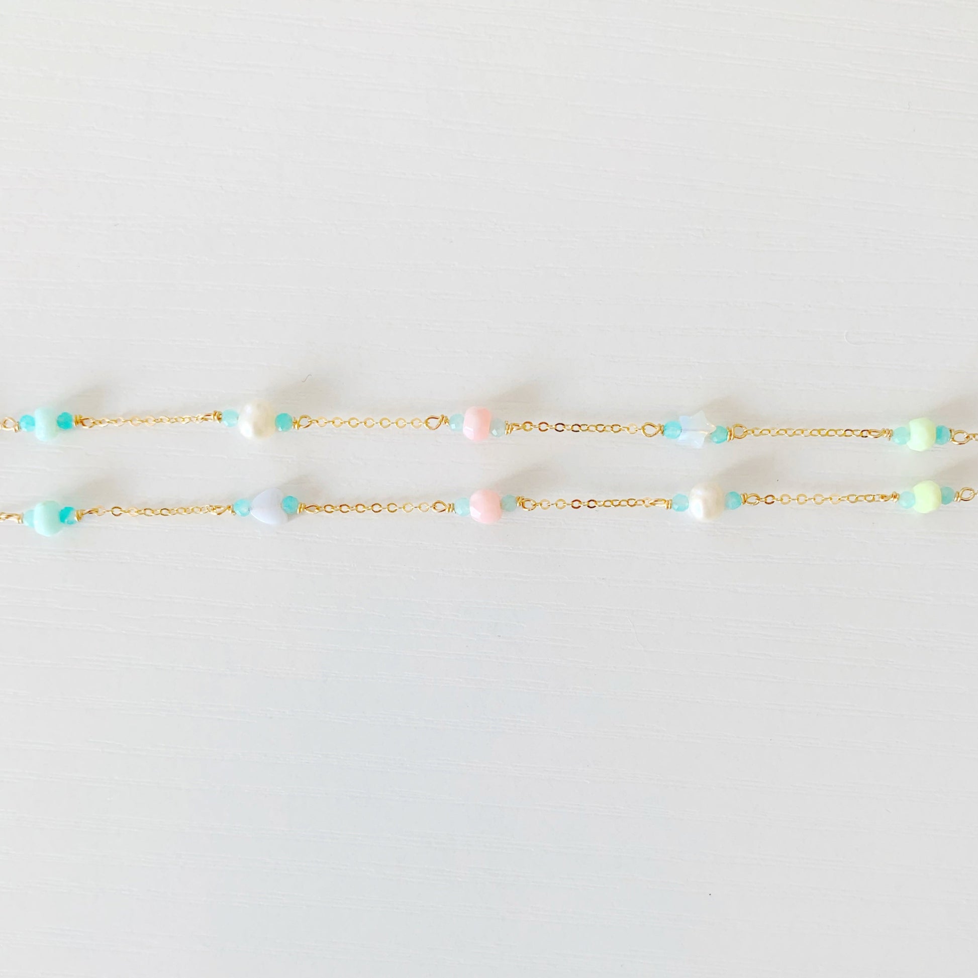 the island hopper necklace by mermaids and madeleines is a station style necklace with a shell at the center and semiprecious beads going up the 14k gold filled chain. this is a photograph of the two sides of the necklace with the semiprecious beads on a white surface