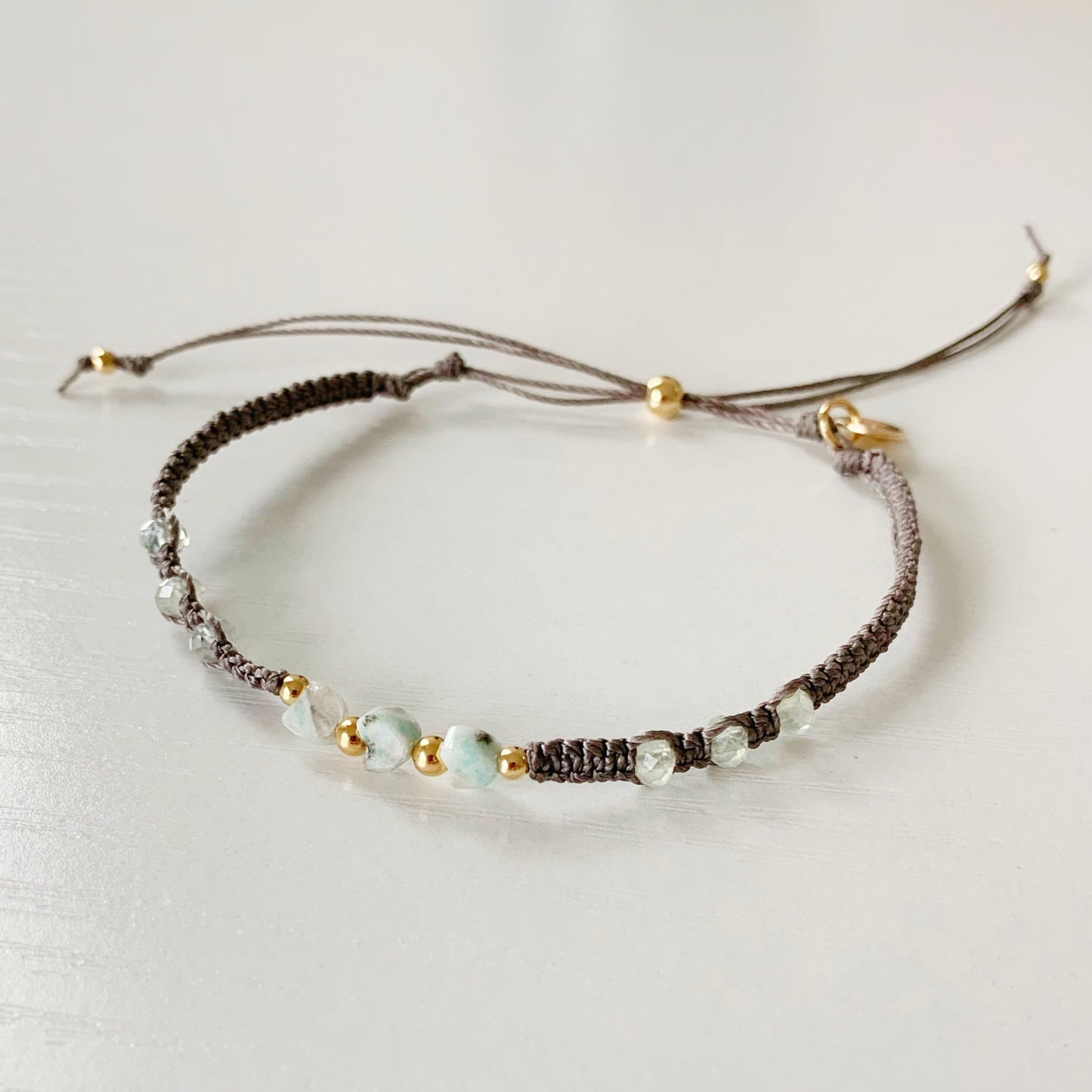 the kiwi cabana bracelet by mermaids and madeleines is a macrame friendship style bracelet with kiwi jasper hearts at the center with 14k gold filled beads, and prehnite beads down the side. this bracelet is photographed close up on a white surface