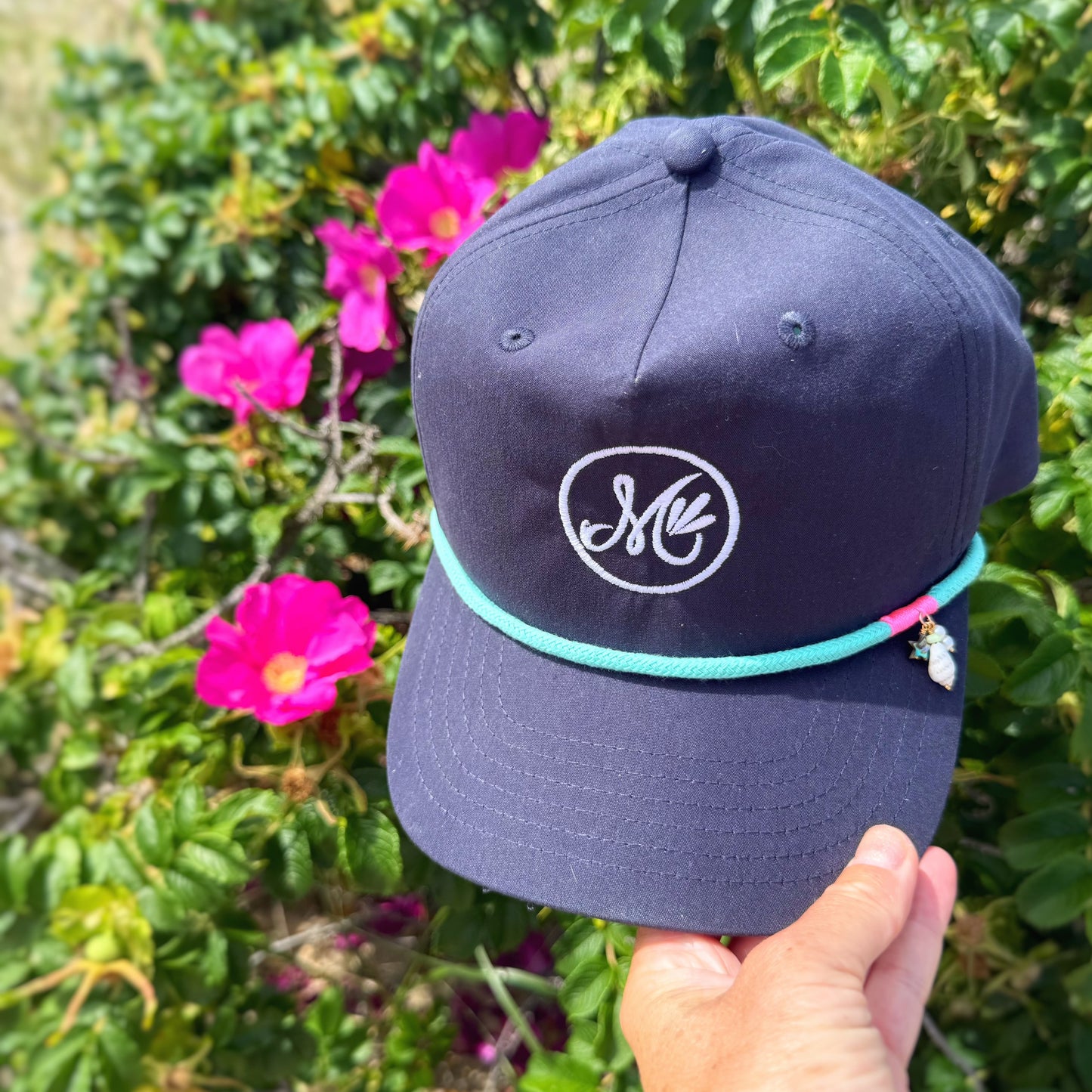 Navy blue cap with a logo held in front of pink flowers and greenery