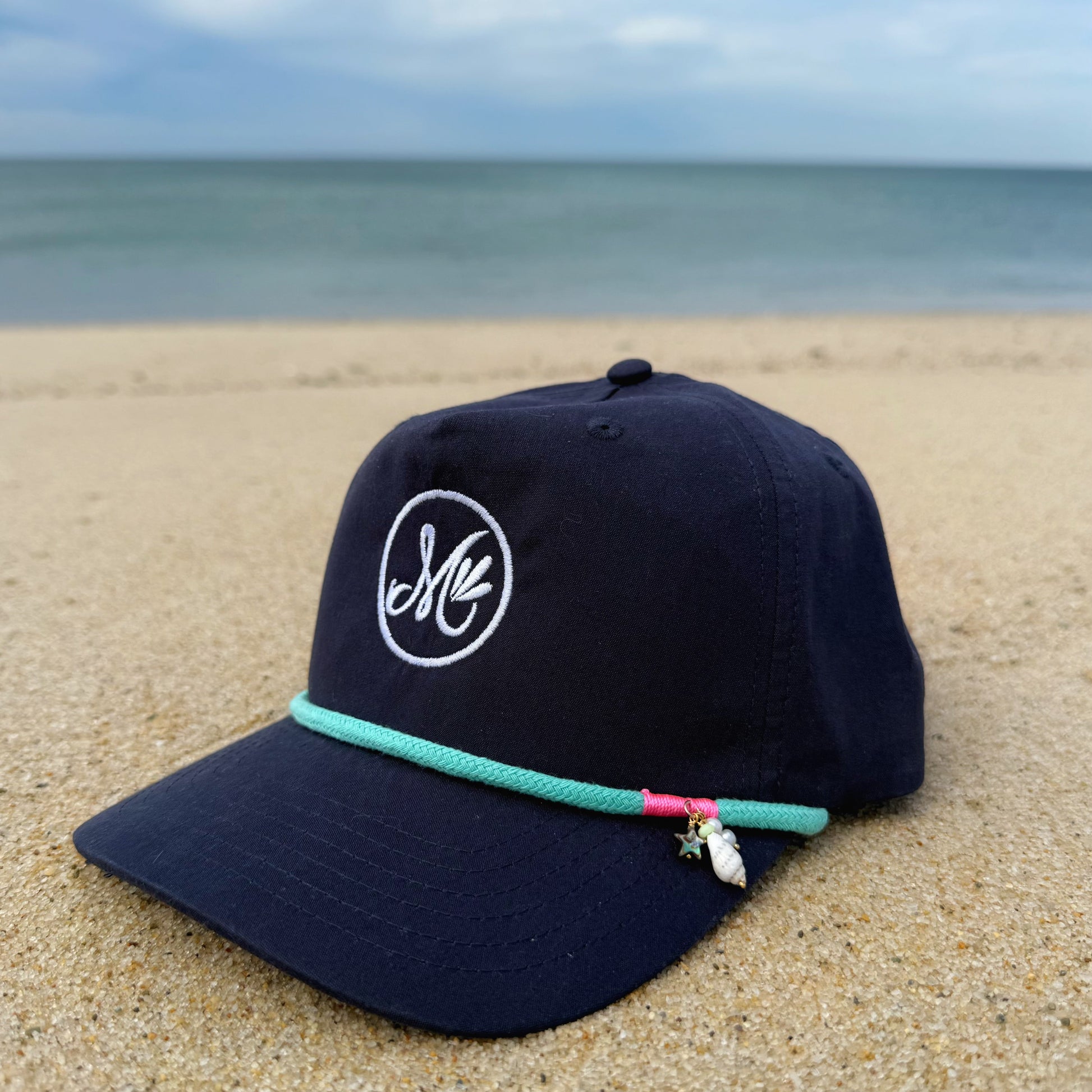 Navy blue cap with a logo on a sandy beach with ocean in the background