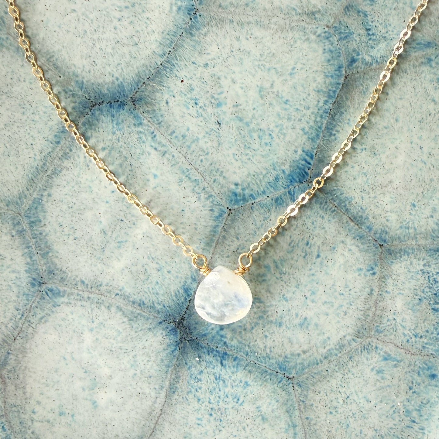 Necklace with a moonstone pendant on a textured blueish gray surface