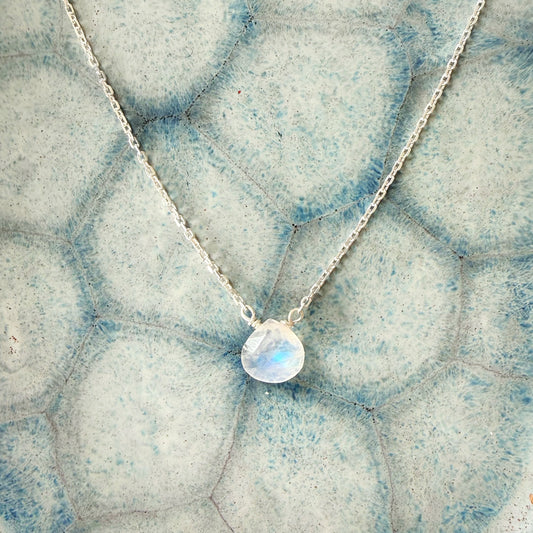 Necklace with a moonstone briolette pendant on a blueish gray textured surface
