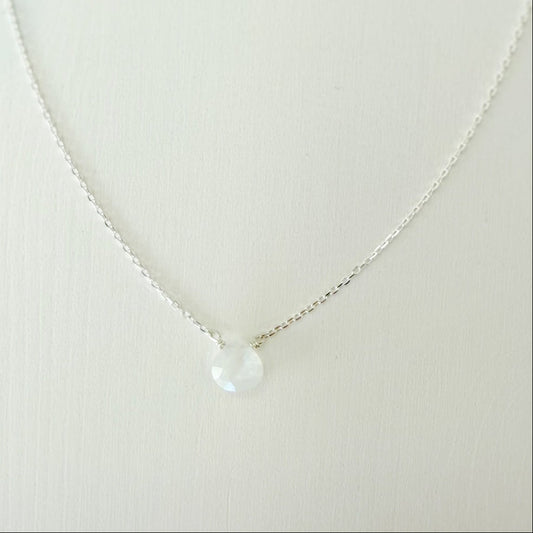 a close up view of the marshmallow necklace by mermaids and madeleines which is a dainty sterling silver chain necklace with a tiny moonstone drop at the center. this necklace is photographed on a white surface