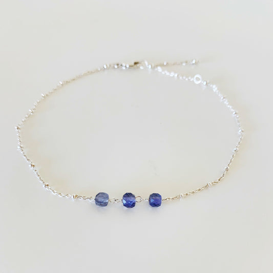 midnight tide anklet by mermaids and madeleines is created with sterling silver dotted chain and 3 iolite faceted cubes at the center of the anklet. this piece is photographed on a white surface