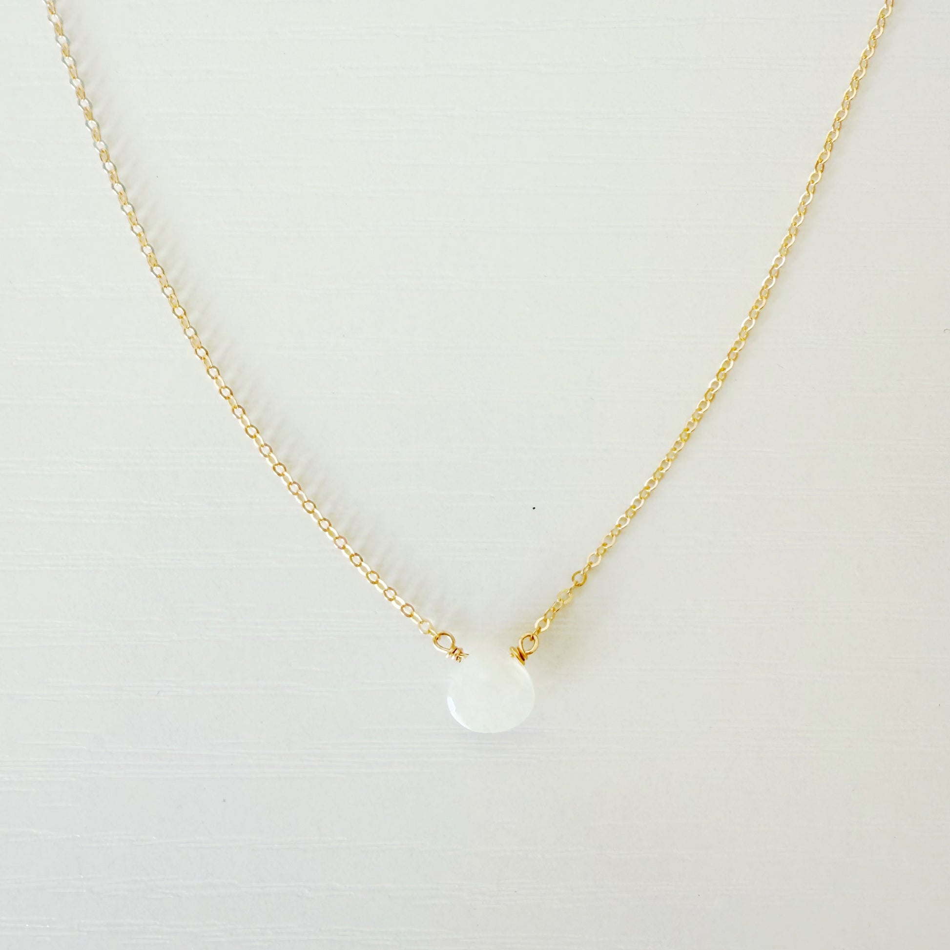 the marshmallow necklace by mermaids and madeleines is a dainty 14k gold filled chain necklace with a tiny moonstone drop at the center. this necklace is photographed close up on a white surface