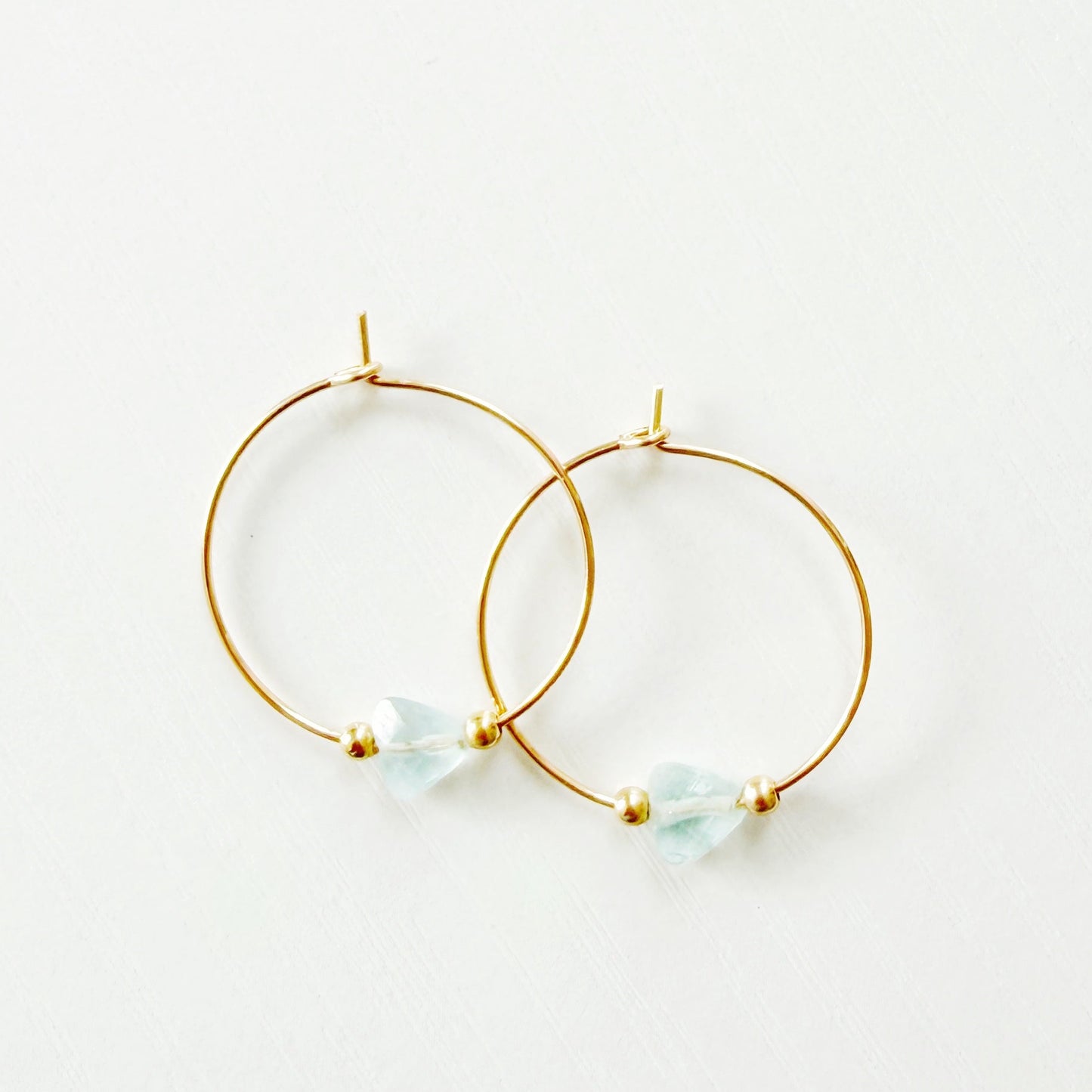 Gold hoop earrings with small triangle aquamarine stones on a white background