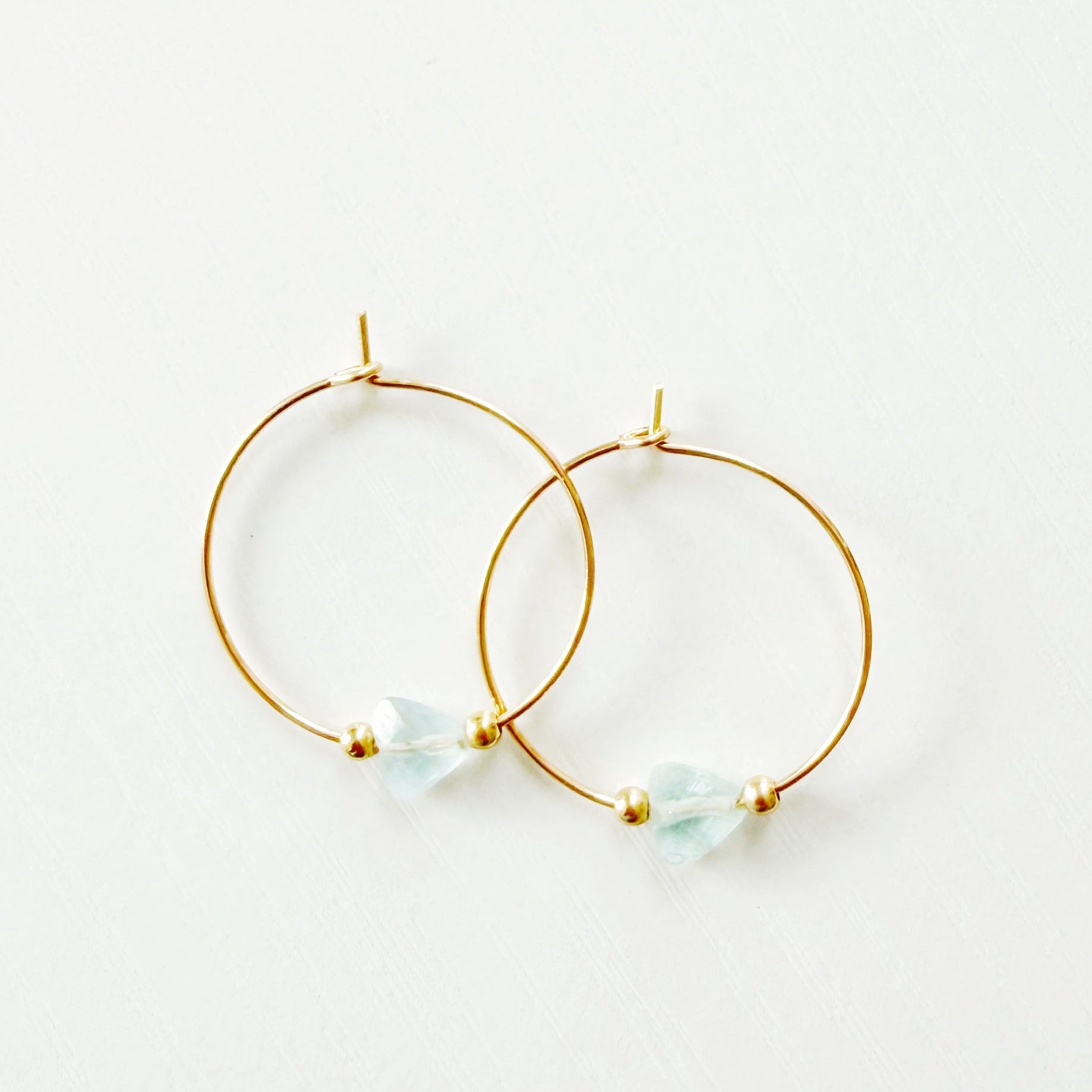 Gold hoop earrings with small triangle aquamarine stones on a white background