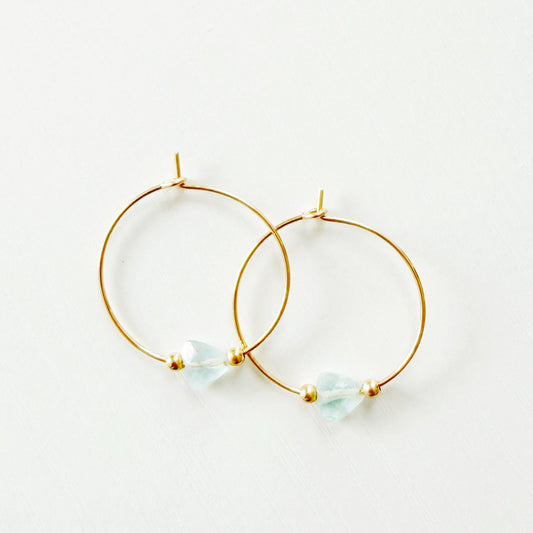 Gold hoop earrings with small triangle aquamarine stones on a white background