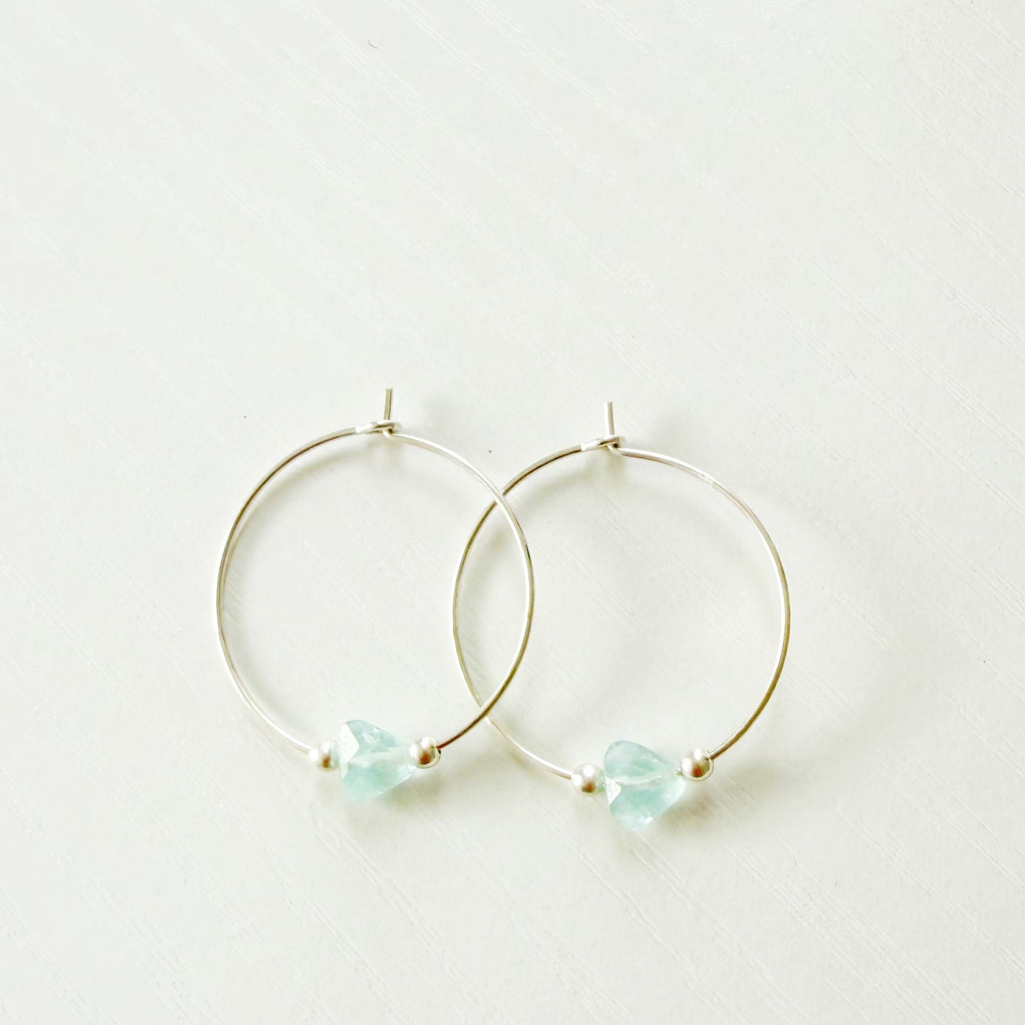 sterling silver hoop earrings with light blue gemstones on a white background