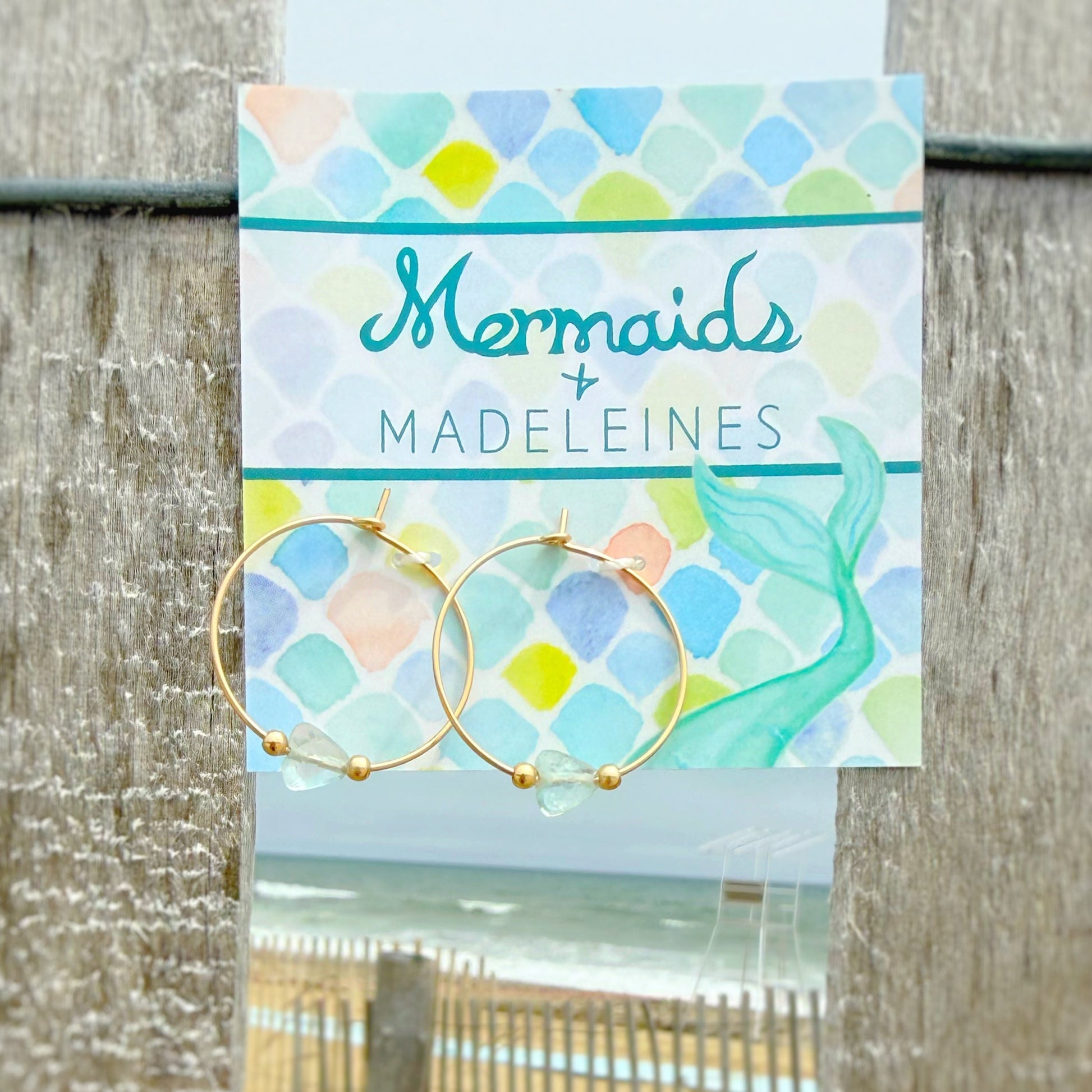 Earring card with mermaid-themed design and beach scene in the background