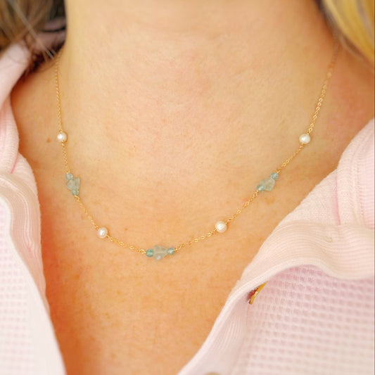 Necklace with small light blue and teal beads and pearls worn by a person