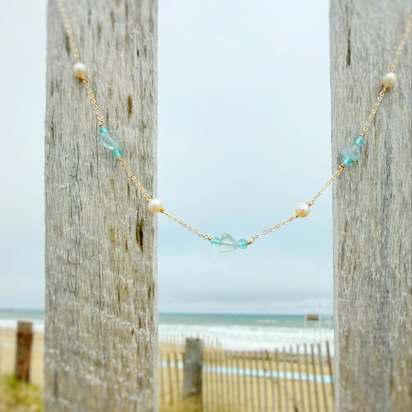 Necklace with beads hanging between two wooden posts with a beach in the background