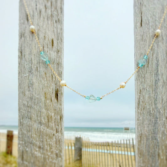 Necklace with beads hanging between two wooden posts with a beach in the background