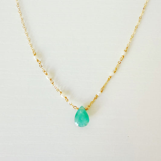 the sea salt necklace by mermaids and madeleines is a pendant style necklace with 14k gold filled chain and a grandidierite drop at the center with a few seed pearls on either side on the chain. this necklace is photographed close up on a white surface