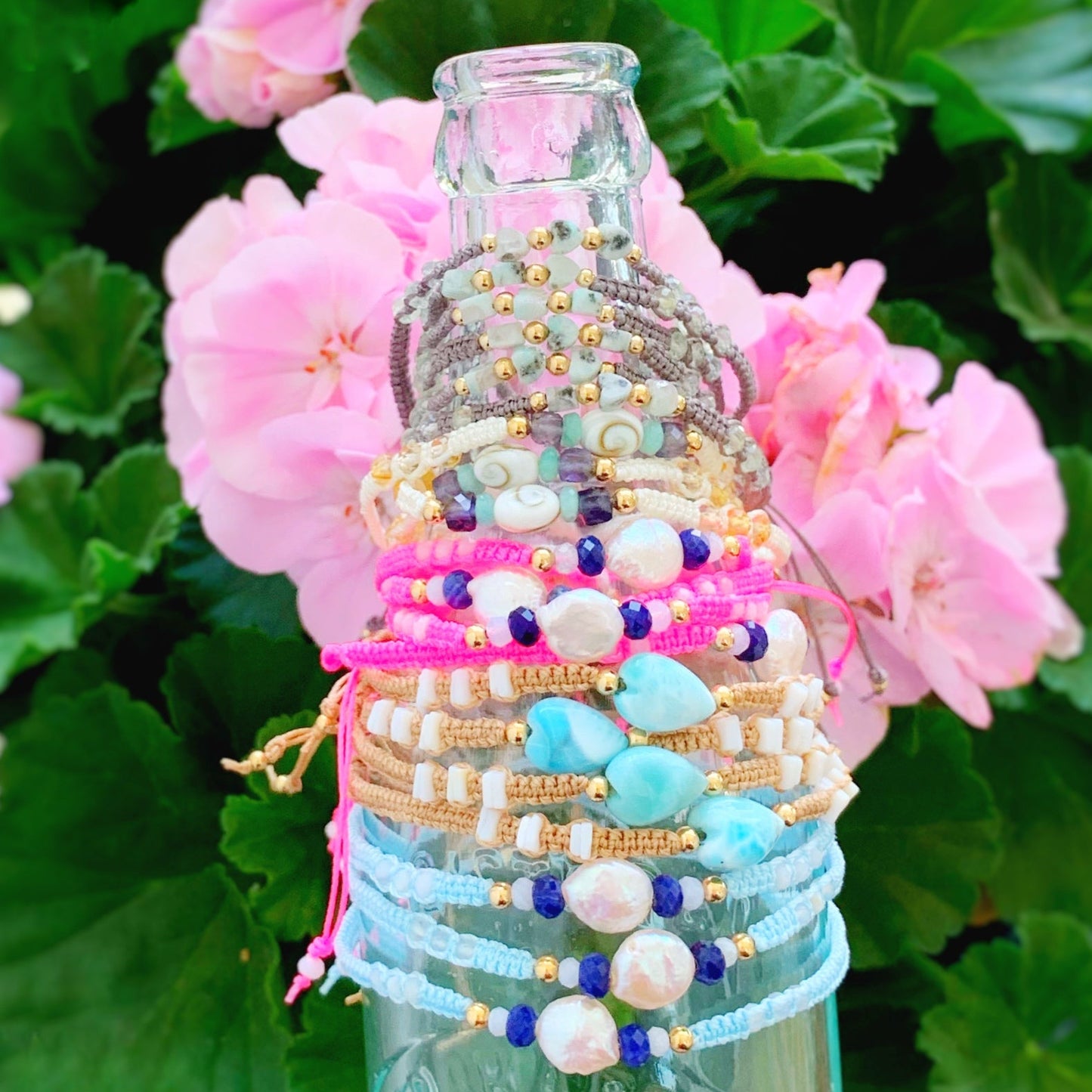macrame adjustable bracelets stacked up on an antique blue bottle in front of pink geraniums 