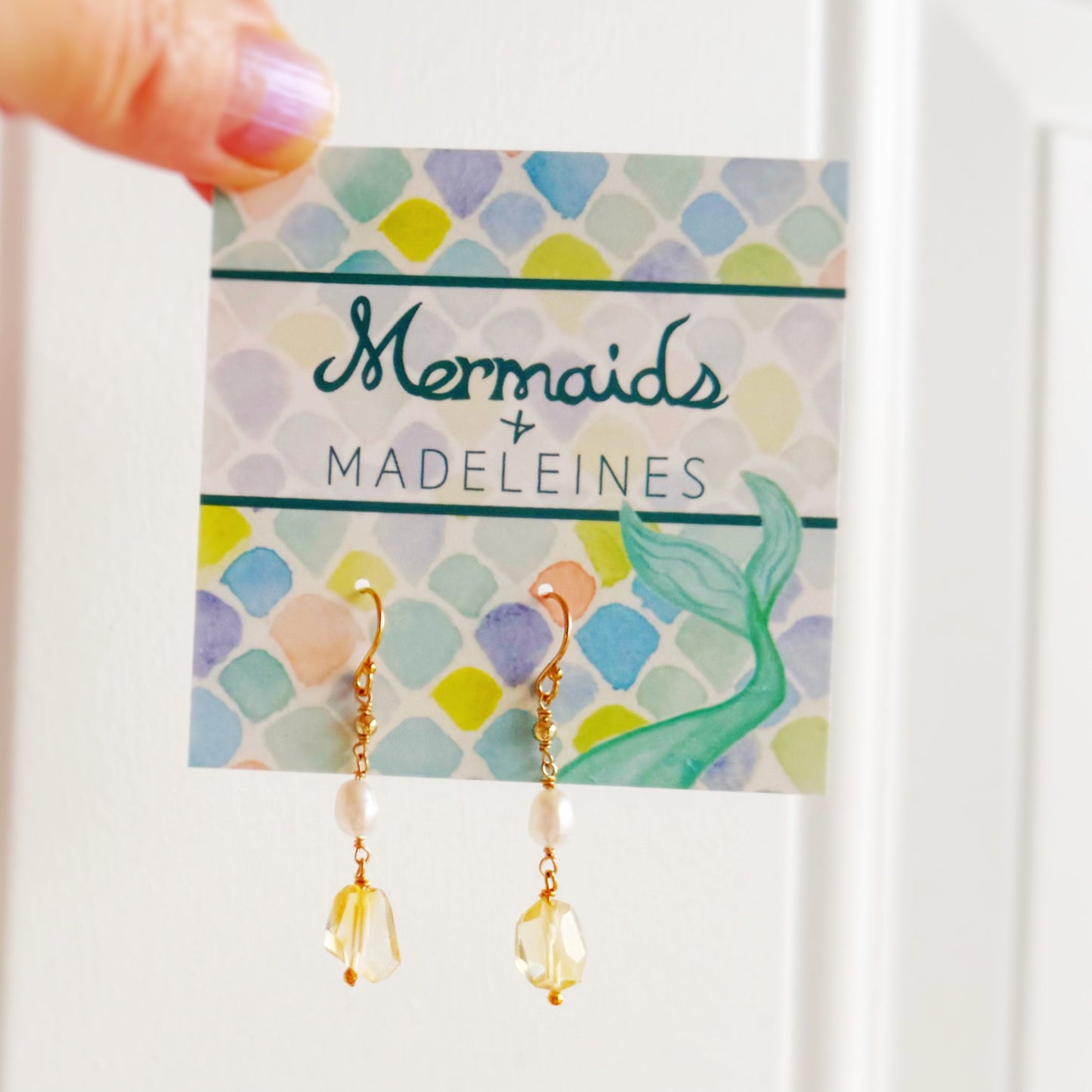 Dangle earrings with pearl and citrine drops made with 14k gold filled metal on a branded card held by a hand.