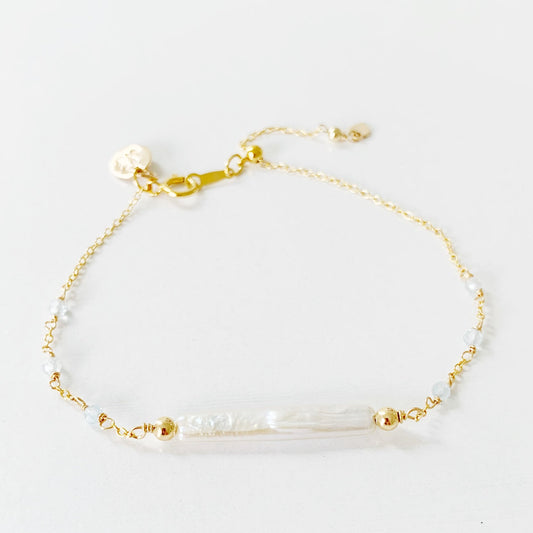 The Truro Adjustable bracelet by mermaids and madeleines features a freshwater stick pearl at the center of the chain bracelet with small microfaceted aquamarine beads on either side. The chain and findings are 14k gold filled with a slide bead near the clasp. this bracelet is photographed on a white surface