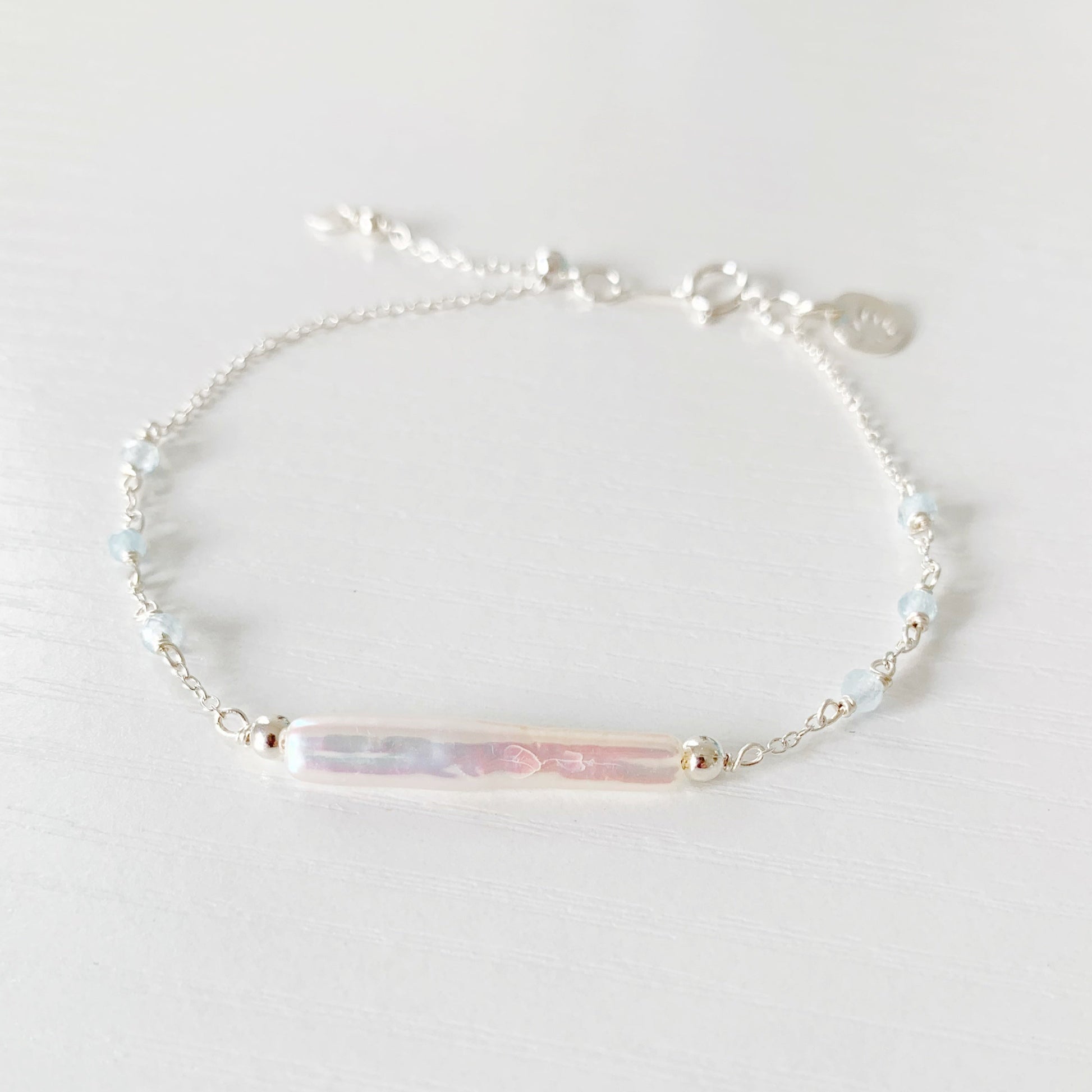 the truro bracelet by mermaids and madeleines is a sterling silver chain bracelet with a freshwater stick pearl at the center and has small faceted aquamarine beads going down the sides with a slide bead near the clasp to make it adjustable. this bracelet is photographed flat on a white surface