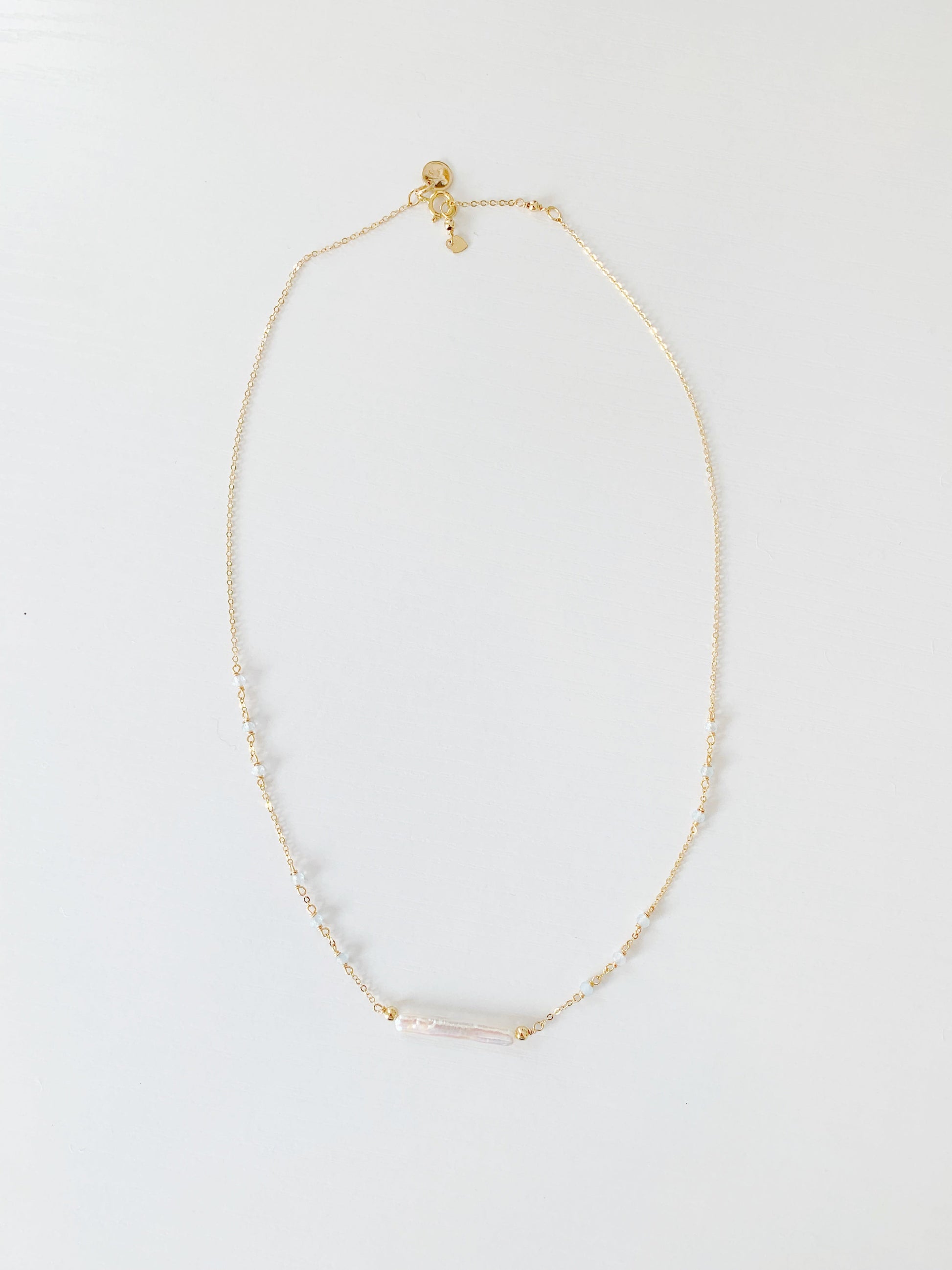 the truro necklace by mermaid and madeleines is a 14k gold filled chain necklace with a freshwater pearl at the center and aquamarine beads going up the sides. this is a photograph of the full length of the necklace on a white surface