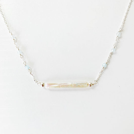 The Truro Necklace by Mermaids and Madeleines features a freshwater stick pearl at the center like a horizontal bar necklace with tiny microfaceted aquamarine beads going up the chain on either side. the chain and findings are sterling silver. this necklace is photographed with just the very front center of the necklace showing and its on a white surface