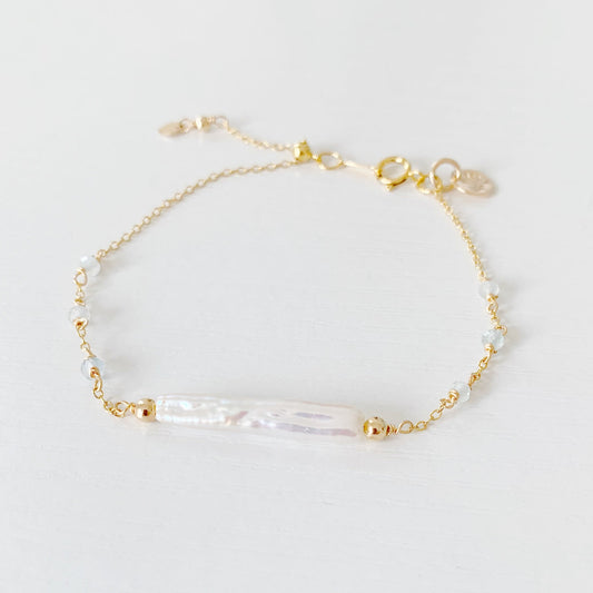 the truro bracelet by mermaids and madeleines is a 14k gold filled chain bracelet with a freshwater stick pearl at the center and aquamarine faceted beads going down the sides. there is a slide bead near the clasp to make the bracelet adjustable. this bracelet is photographed flat on a white surface