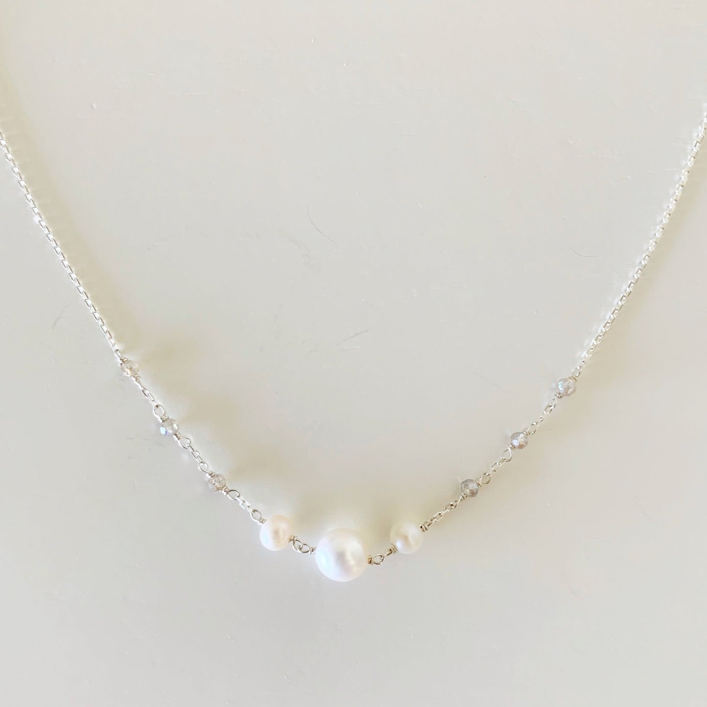 the westport necklace by mermaids and madeleines is created with sterling silver chain with hand wrapped freshwater pearls at the center and labradorite gems on the chain. this necklace is photographed closer up on a white surface