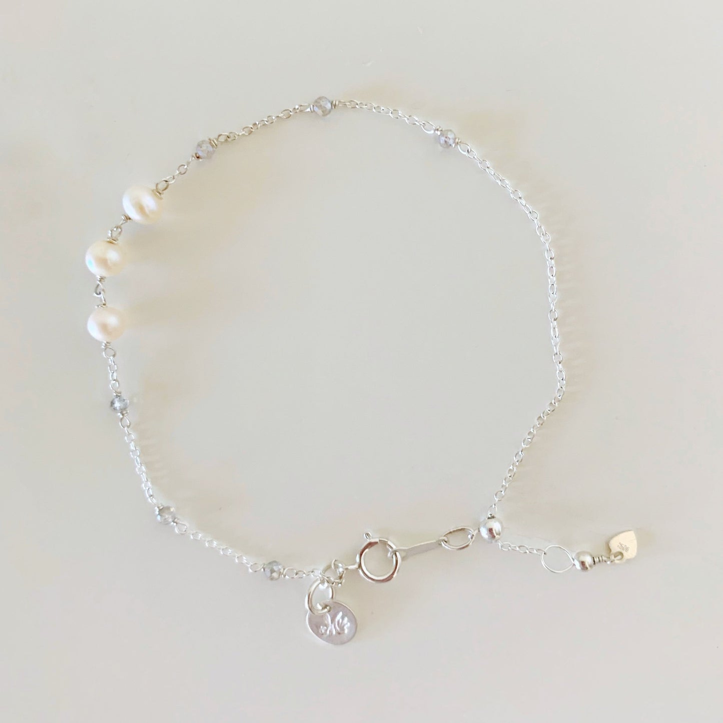 the westport bracelet by mermaids and madeleines is created with freshwater pearls and small labradorite gems hand wrapped on the chain. this adjustable bracelet has a silicone slide bead near the back at the clasp. the westport bracelet here is photographed on a white surface