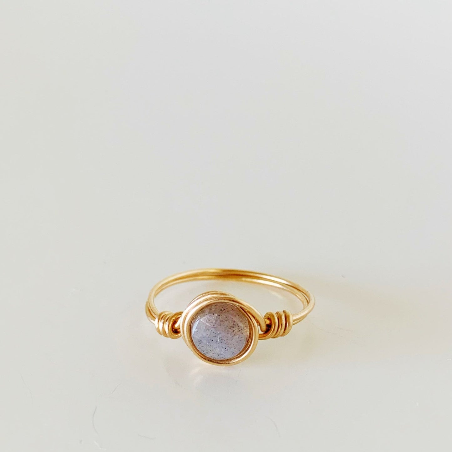 the arctic ring by mermaids and madeleines is a wire wrapped ring made with 14k gold filled wire and a faceted coin labradorite bead at the center. this ring is facing forwards and photographed on a white surface