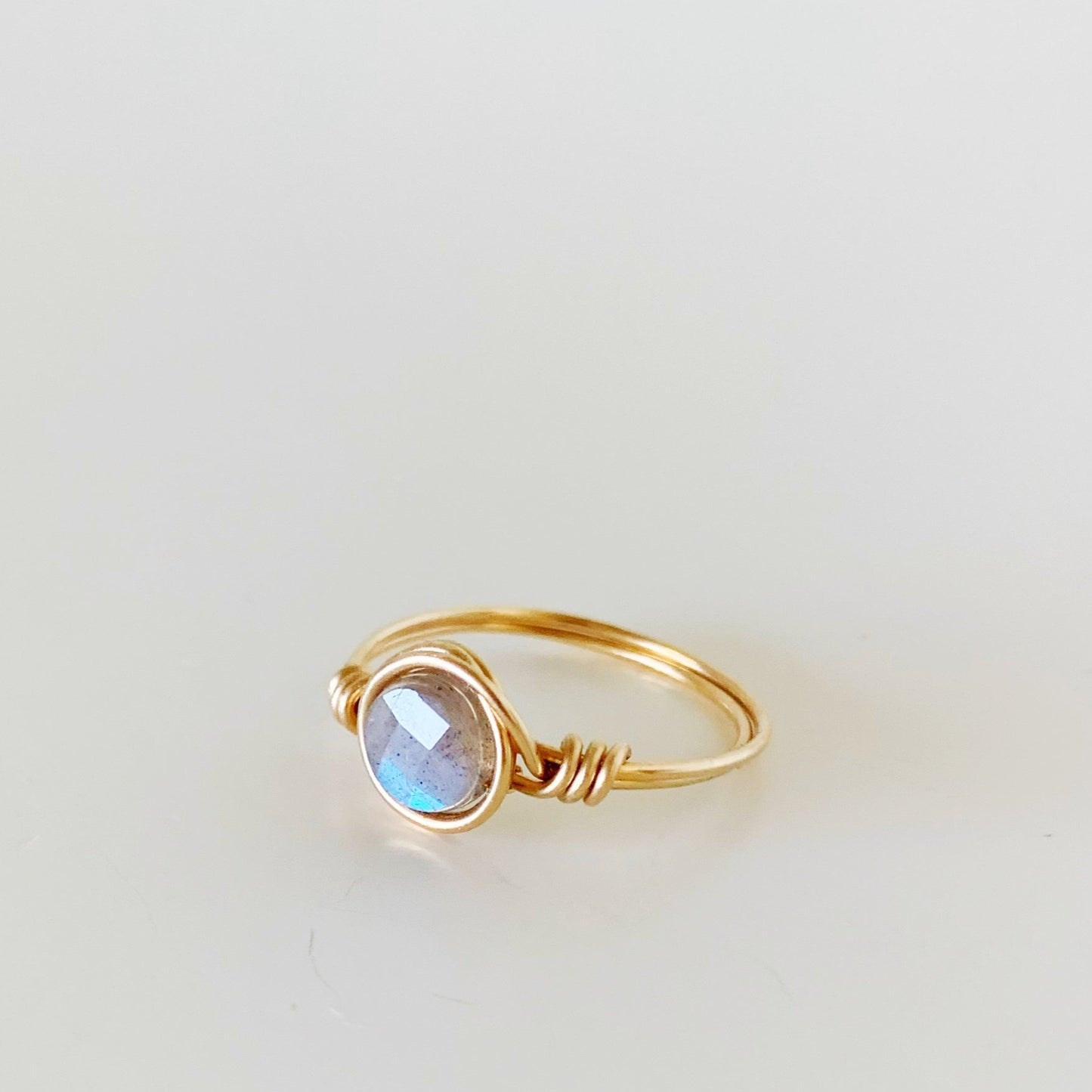 the mermaids and madeleines arctic ring is a wire wrapped ring made with 14k gold filled wire and a faceted labradorite coin bead at the center. this ring is facing to the left to show a side view and is photographed on a white background