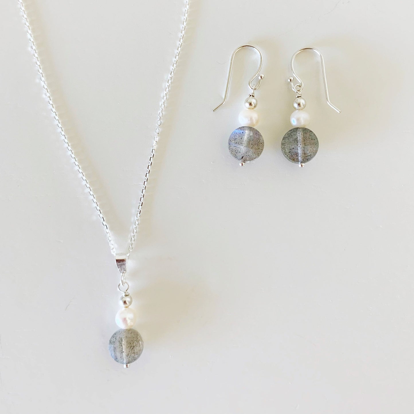 Arctic pendant necklace and earrings by mermaids and madeleines are created with freshwater pearl and faceted labradorite coins with sterling silver findings and chain. this set is photographed ona white surface