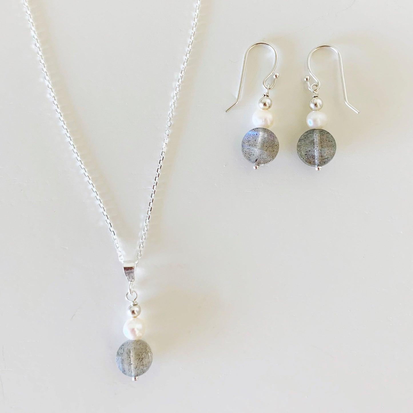 The arctic pendant necklace and earrings by mermaids and madeleines are created with small freshwater pearls, faceted labradorite coins and sterling silver chain and findings. this set is photographed on a white background