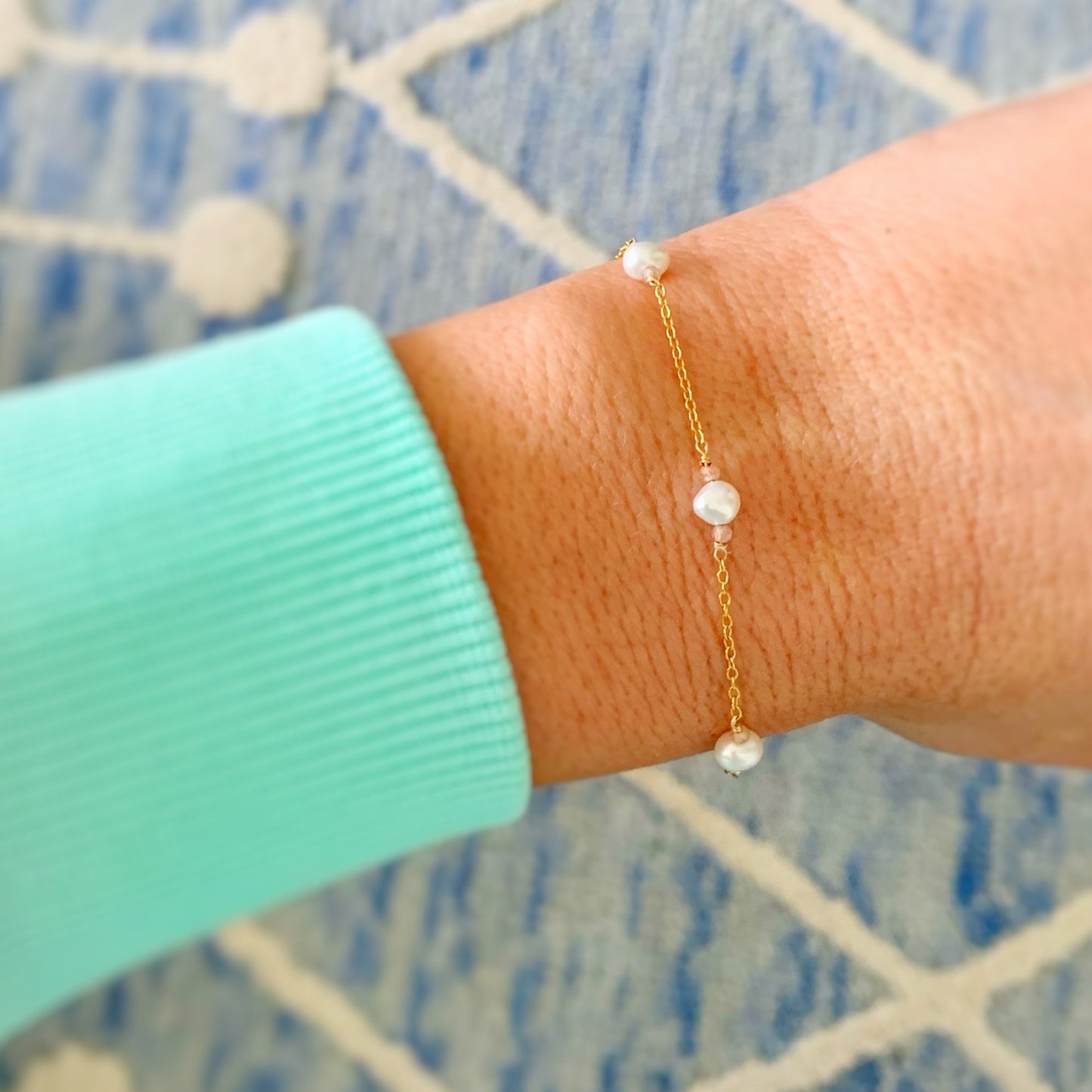 the mermaids and madeleines bristol bracelet is created with 14k gold filled chain, freshwater pearls and peach moonstone in a station style bracelet with an adjustable clasp. this is a photograph of the bracelet on a wrist