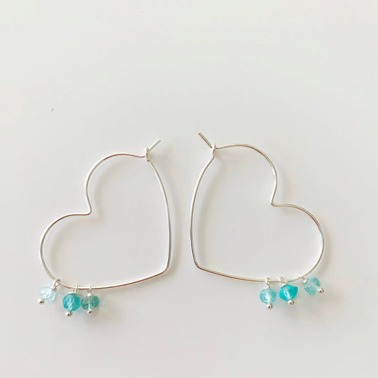 the beach lover earrings by mermaids and madeleines are heart shaped hoop earrings designed with sterling silver wire and apatite bead drops. this pair is photographed on a white surface