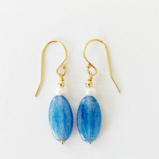 the brewster earrings by mermaids and madeleines are long oval blue kyanite beads with small pearls on top before the 14k gold filled findings. this pair is photographed flat on a white surface