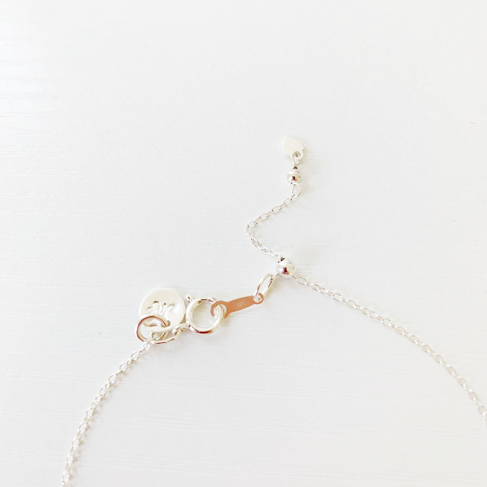 the brewster bracelet by mermaids and madeleines is an adjustable sterling silver chain bracelet with a slide bead at the clasp. there's a blue kyanite coin bead at the center complimented by small freshwater pearls on each side. this is a photo of just the back of the bracelet on a white surface to just show how the slide clasp works