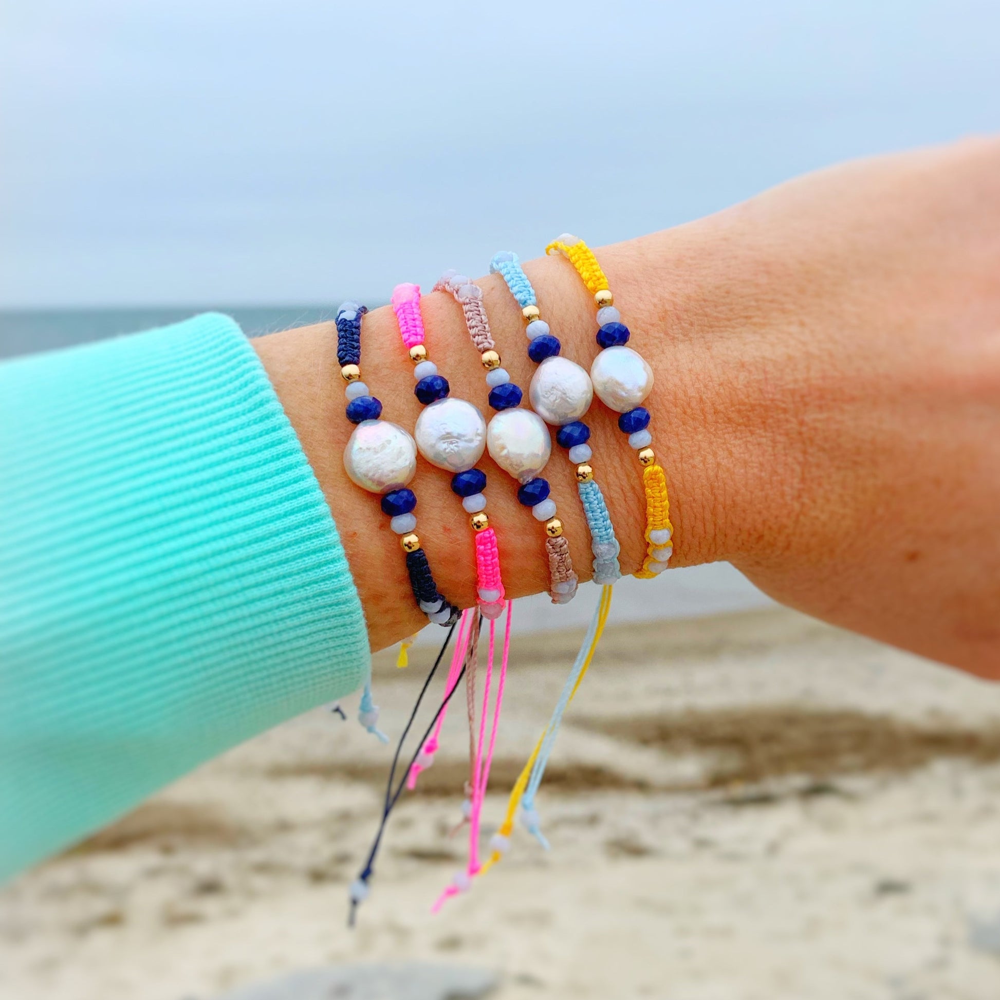 all 5 available colors of the bristol bracelets worn on a wrist in front of the ocean background