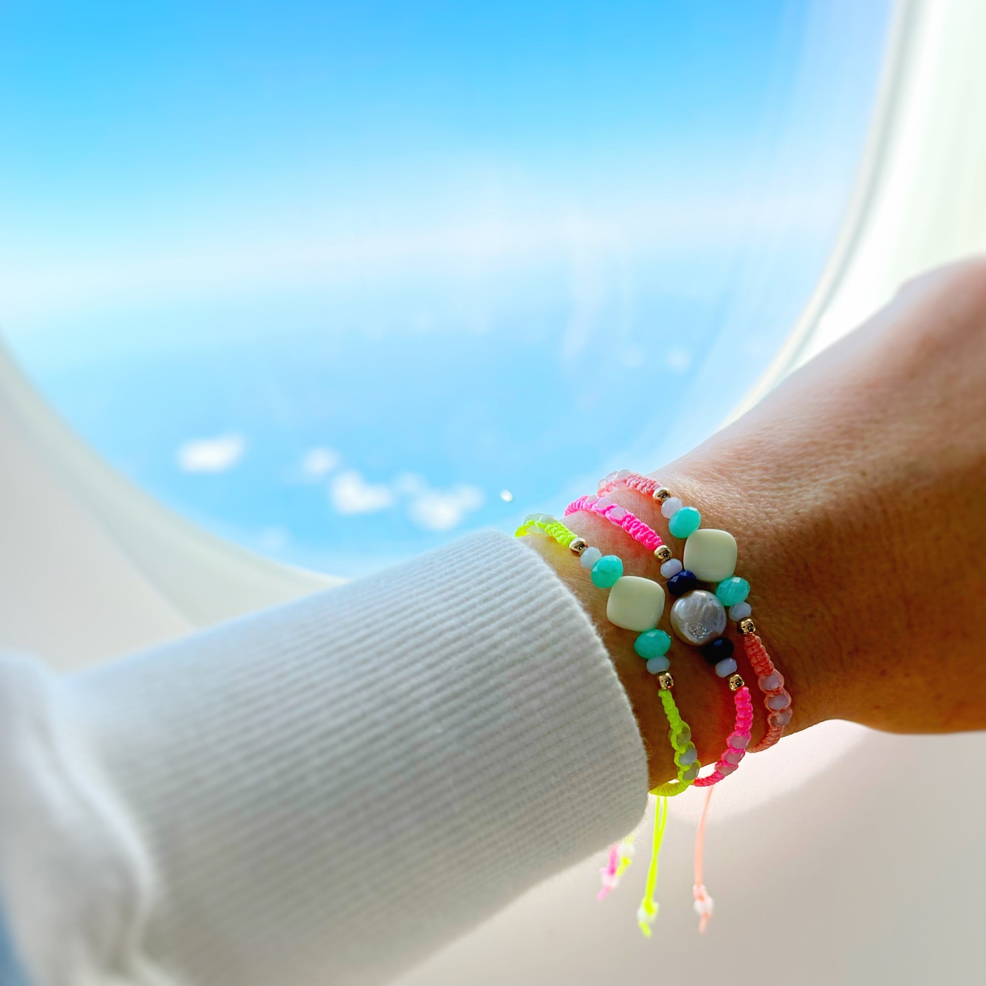 Colorful beaded bracelets on a wrist with a bright blue sky background from an airplane window