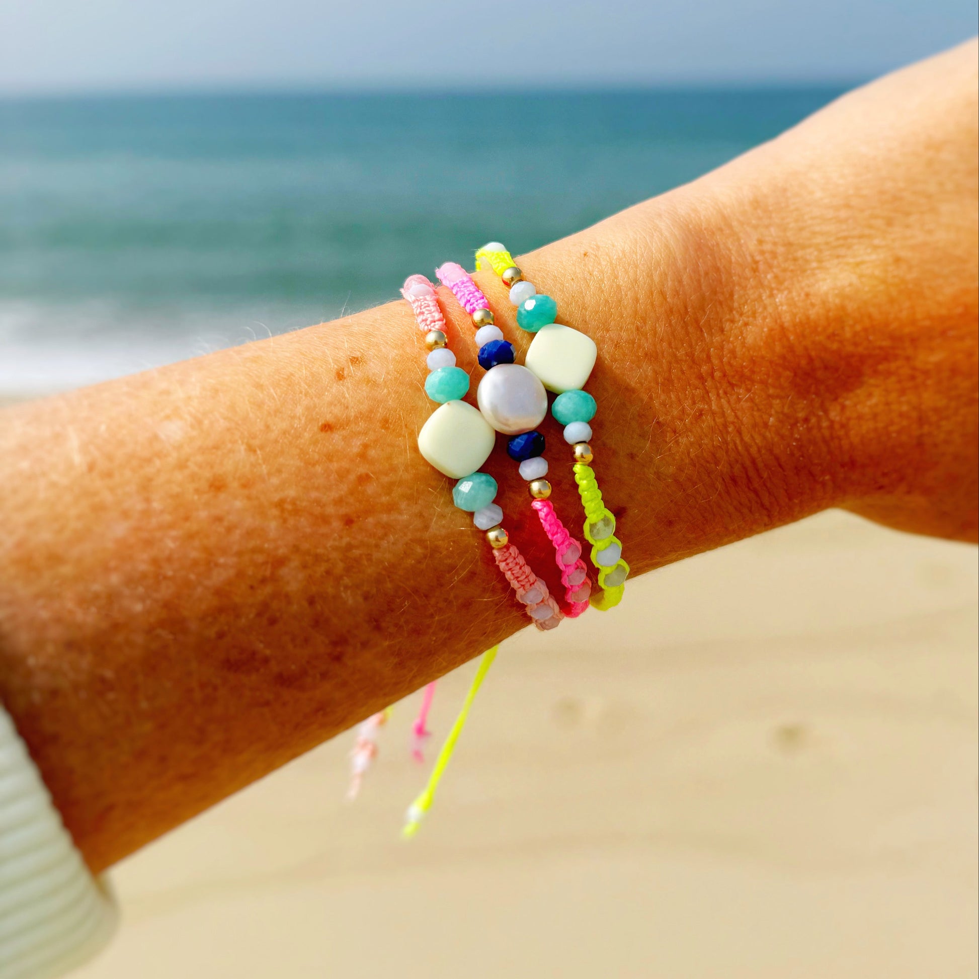 Colorful beaded and macrame bracelets on a wrist with a beach background