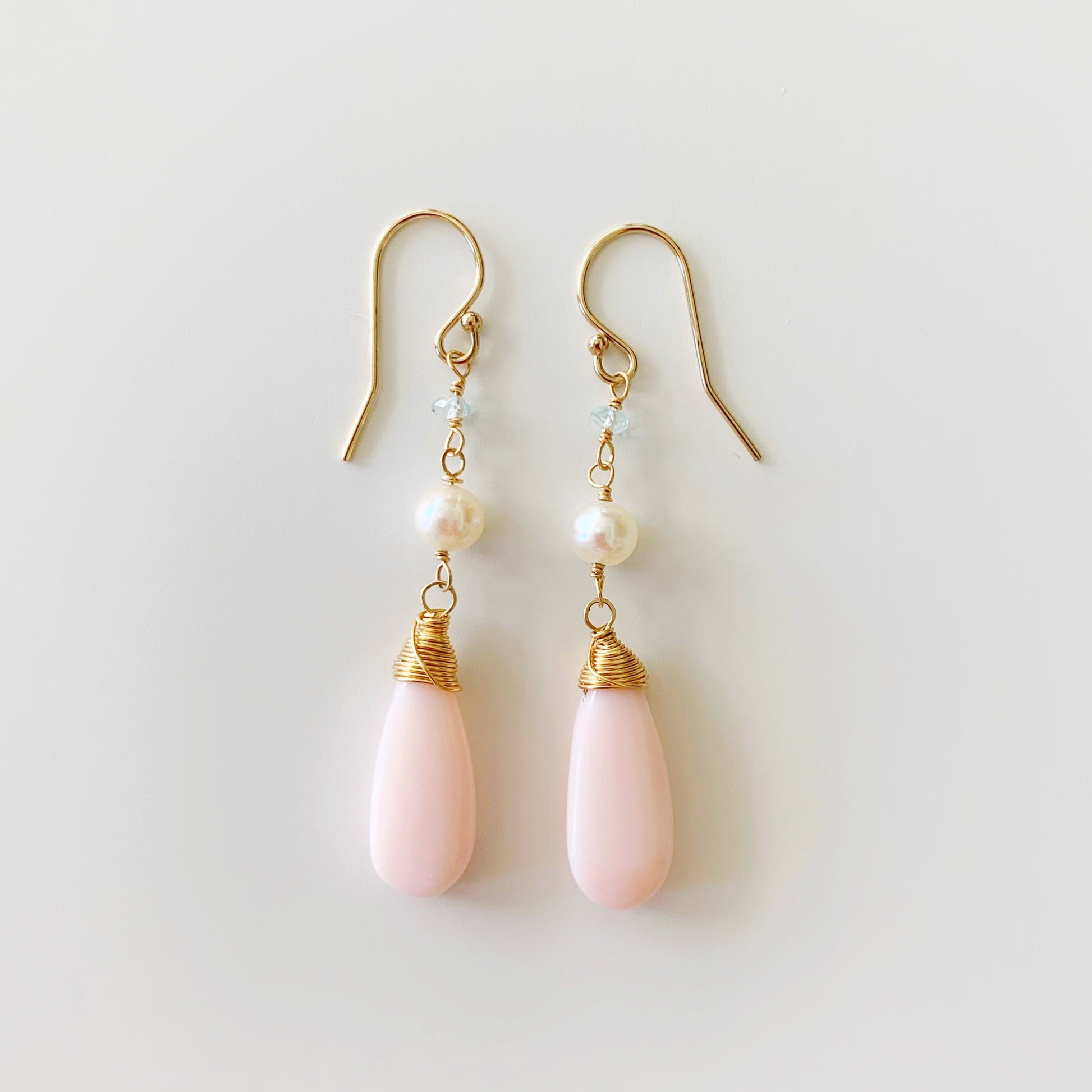 the cotton candy sky earrings by mermaids and madeleines are linear style long earrings with pink opal long drops and freshwater pearl and tiny aquamarine beads with 14k gold filled findings. this pair is photographed flat on a white surface