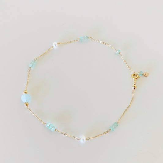 go with the flow anklet by mermaids and madeleines is designed with dainty gold chain with stations of aqumarine, green amethyst, and freshwater pearl. this anklet is photographed flat on a white surface