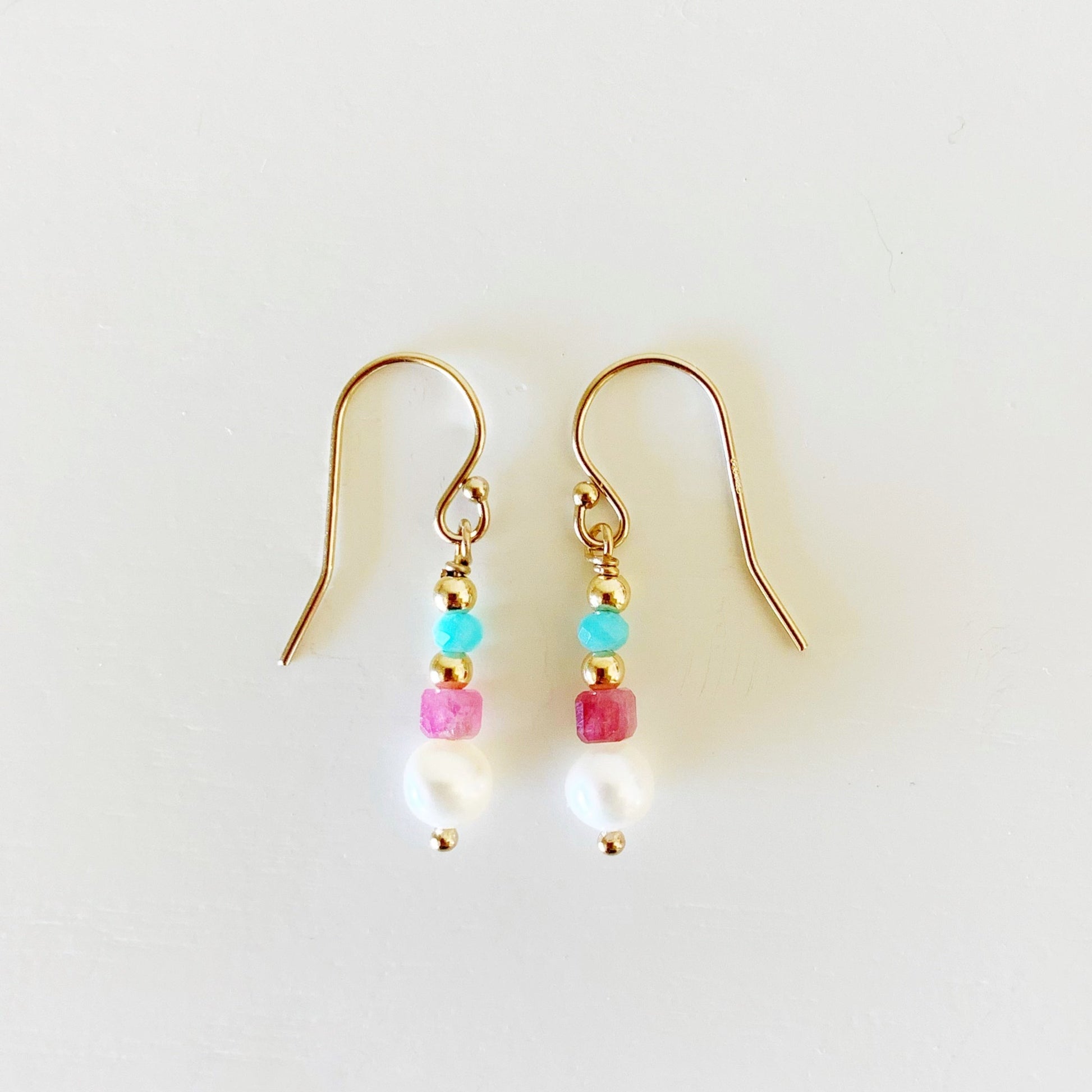 the harwich port earrings by mermaids and madeleines are petite linear earrings with freshwater pearls, faceted cube shaped pink tourmaline beads and bright microfaceted amazonite rondelles on 14k gold filled findings. this pair of earrings is photographed flat on a white surface