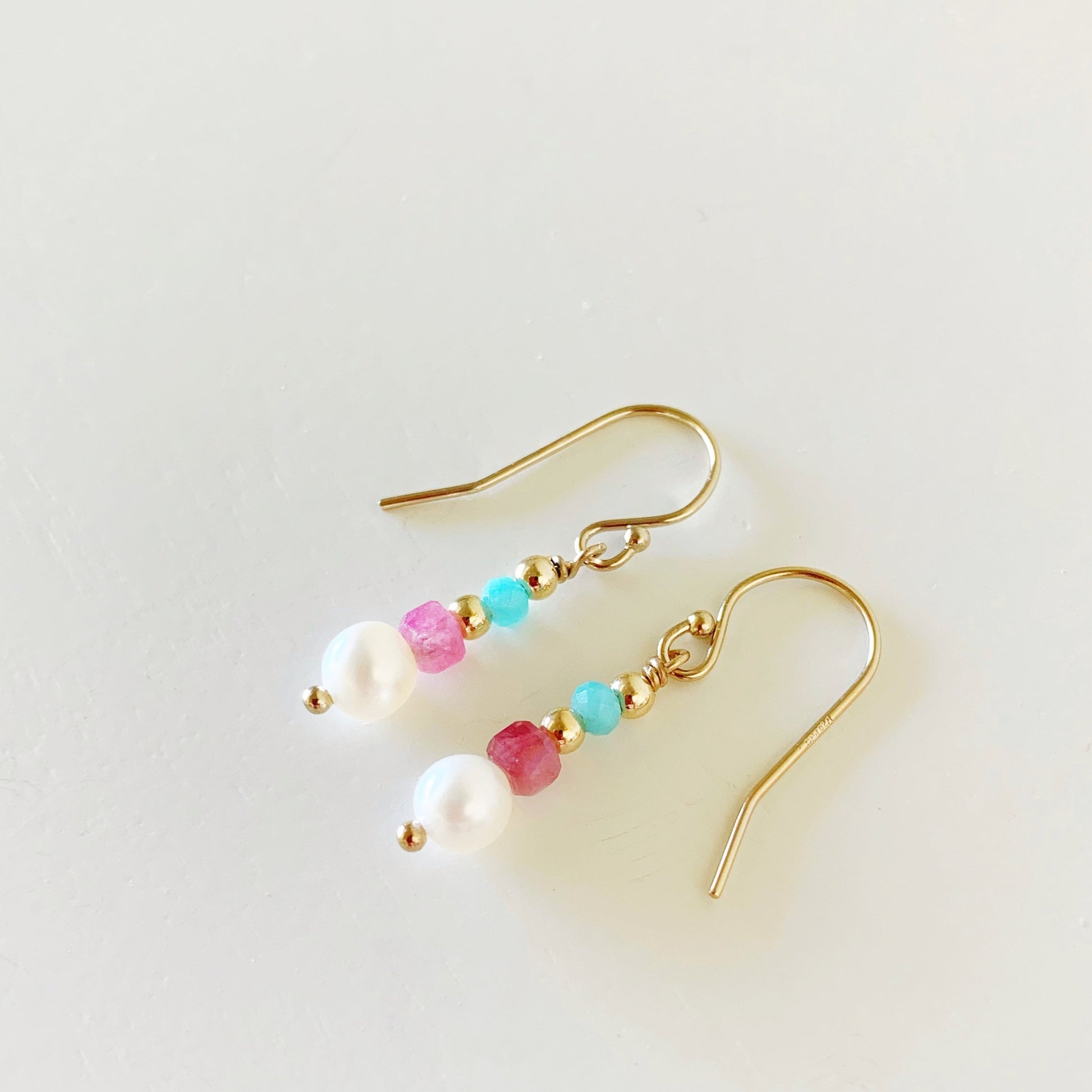 the harwich port earrings by mermaids and madeleines are created with 14k gold filled beads and findings, with freshwater pearls, faceted pink tourmaline beads and bright amazonite rondelles. these earrings are a petite linear style. the earrings are pointing to the left and photographed flat on a white surface
