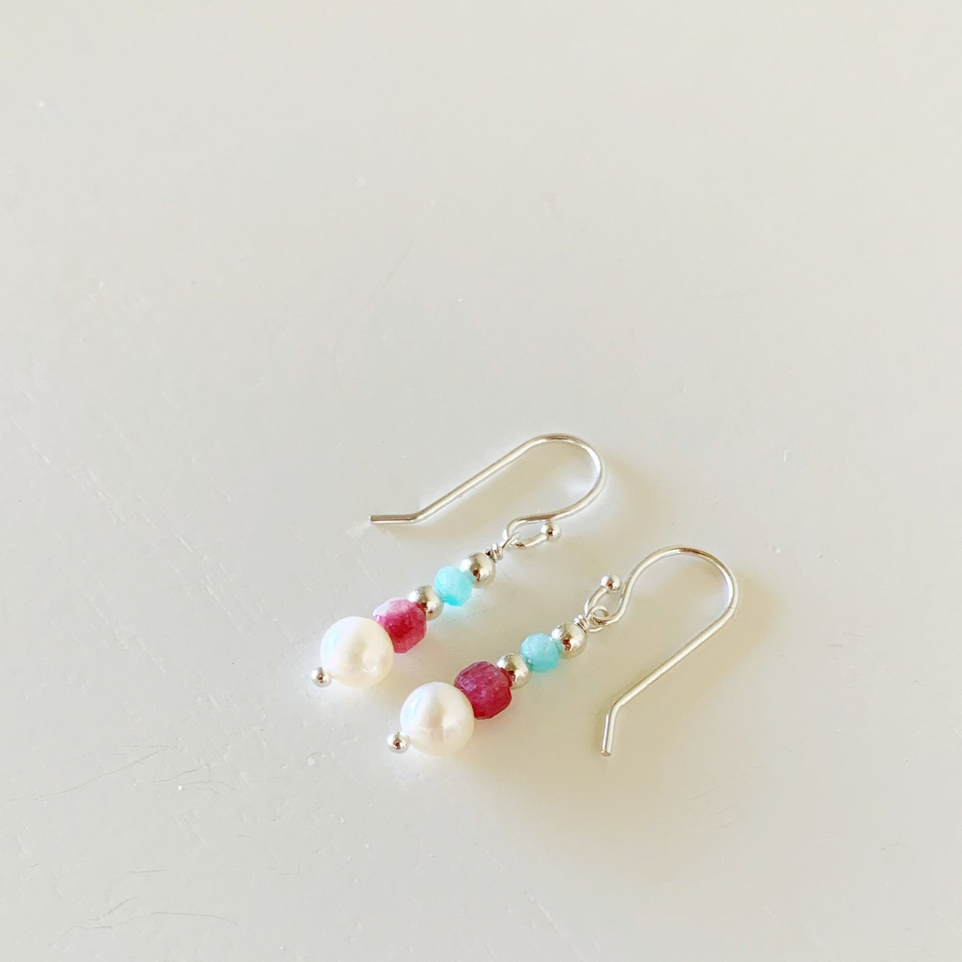 the harwich port earrings by mermaids and madeleines are a petite linear style designed with freshwater pearls, pink tourmaline cube beads and amazonite rondelles with sterling silver findings. this pair of earrings is facing to the left and photographed flat on a white surface
