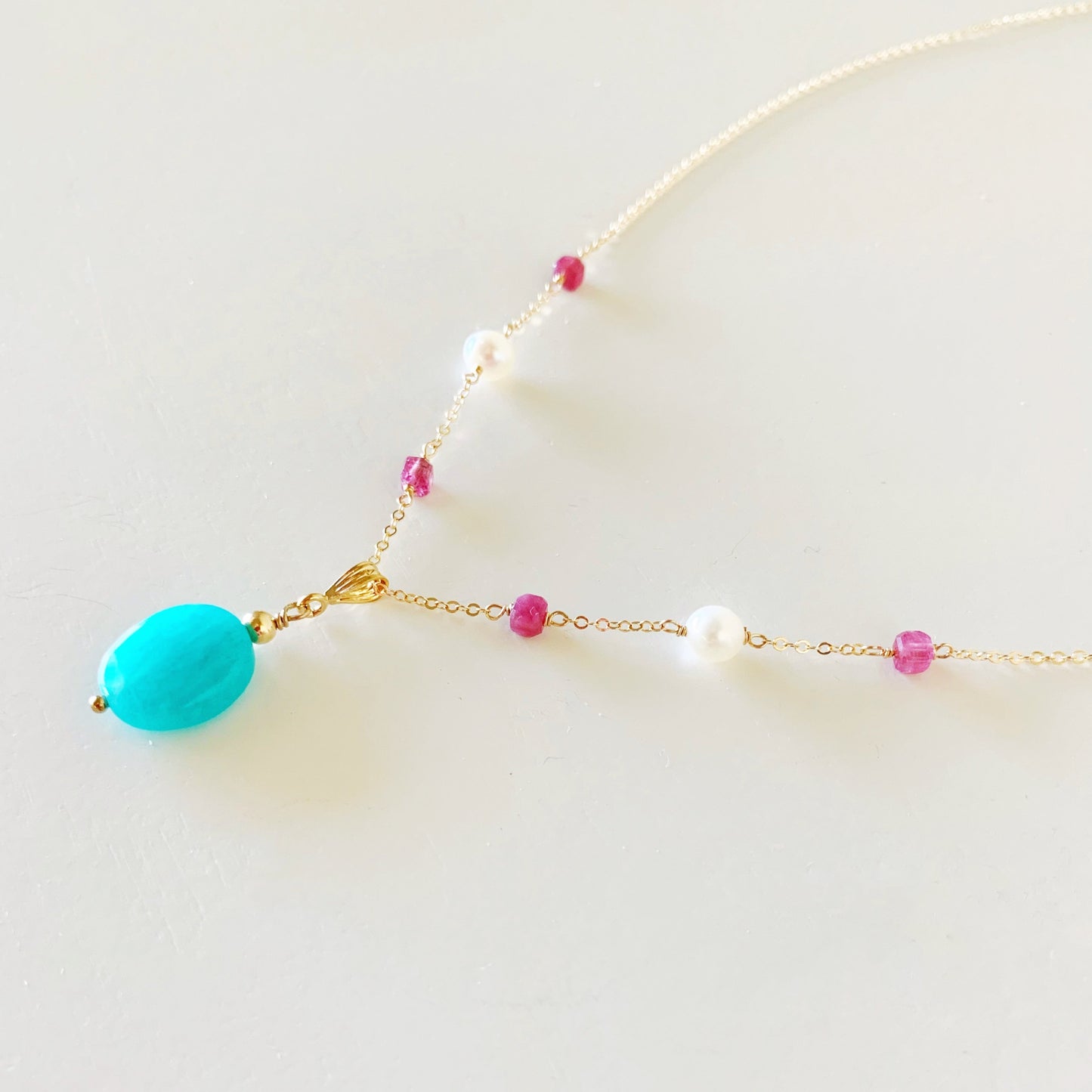 the harwich port by mermaids and madeleines is a pendant design with a bright amazonite stone suspended from 14k gold filled chain that has pink tourmaline and freshwater pearl on the chain. this necklace is facing to the left  and photographed on a white surface