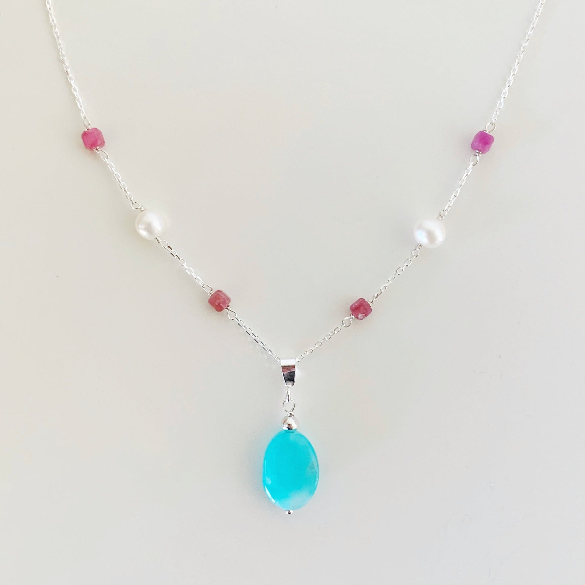the harwich port necklace by mermaids and madeleines is a pendant style necklace with bright amazonite suspended from sterling silver chain with pink tourmaline and freshwater pearls. this necklace is viewed closer up and is photographed on a white surface