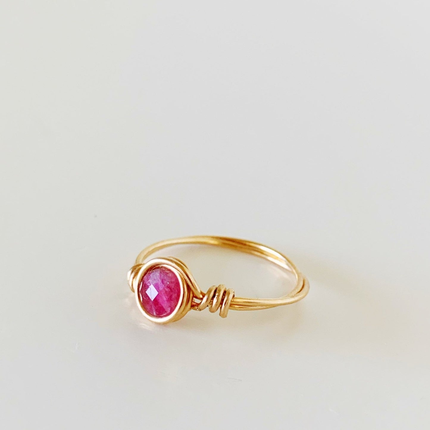 the harwich port ring by mermaids and madeleines is a wire wrapped ring created with 14k gold filled wire with a faceted pink tourmaline coin bead at the center. this ring is facing to the left and photographed on a white surface